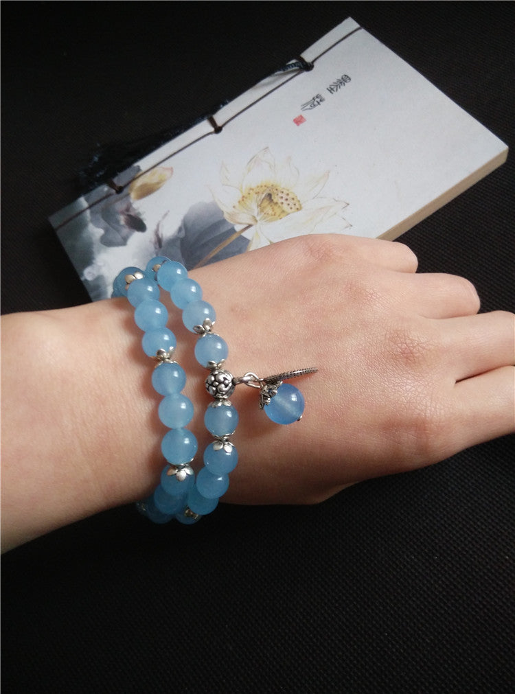 Hand wearing a blue beaded bracelet with a dark background