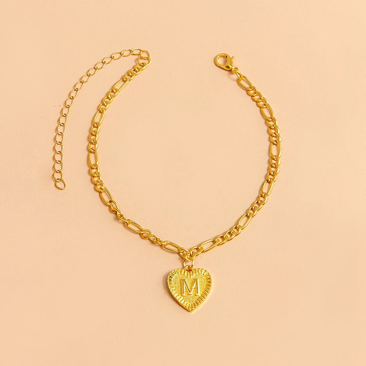 Gold bracelet with a heart-shaped pendant letter M on a beige background