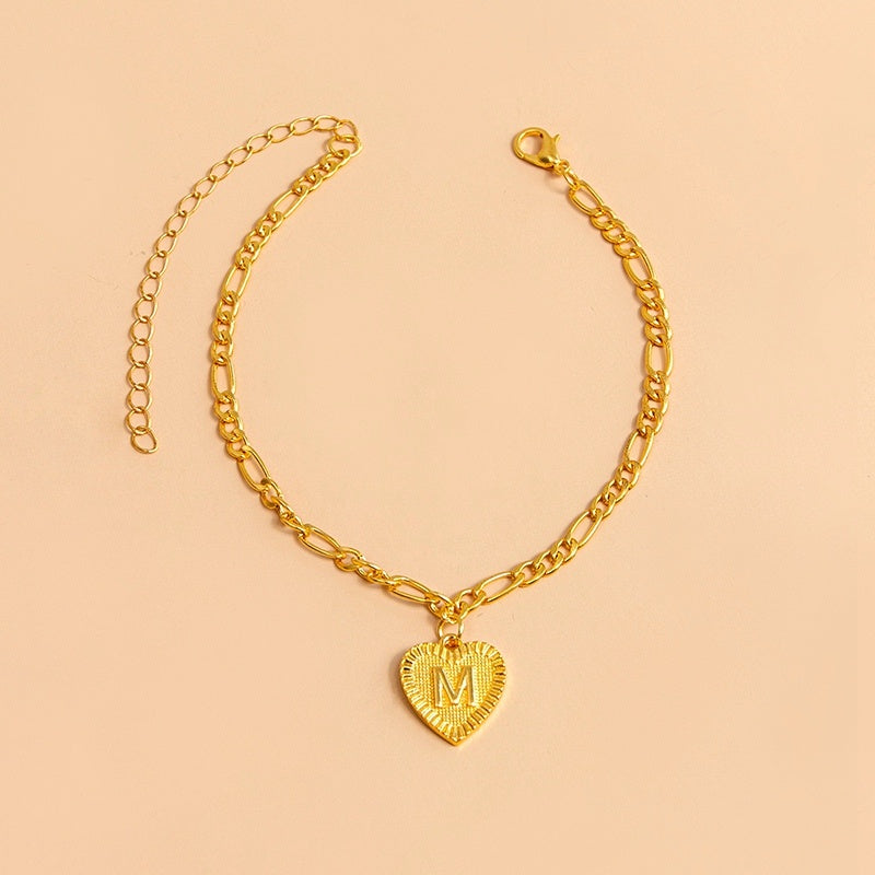 Gold bracelet with a heart-shaped pendant letter M on a beige background