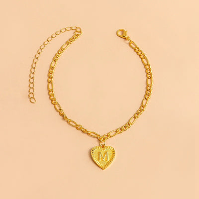 Gold bracelet with a heart-shaped pendant letter M on a beige background