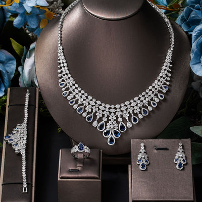 Blue zircon bridal Jewelry set including necklace, bracelet, ring, and earrings on a mannequin bust with flowers in the background.