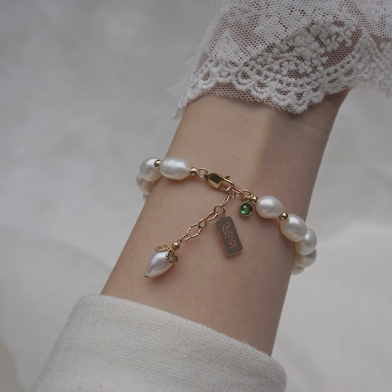 Pearl bracelet with charms on a wrist against a neutral background