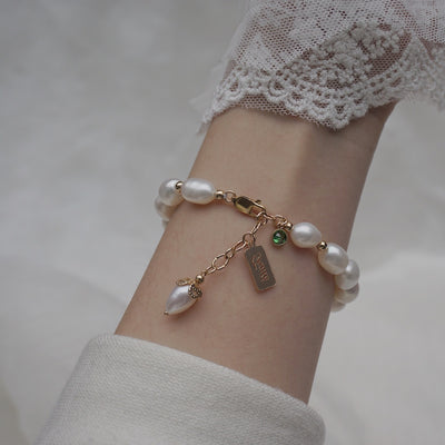 Pearl bracelet with charms on a wrist against a neutral background