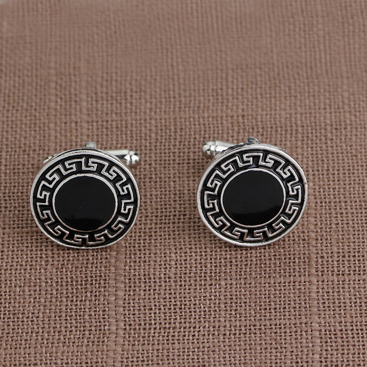 Round cufflinks with black center and decorative border on a brown fabric background