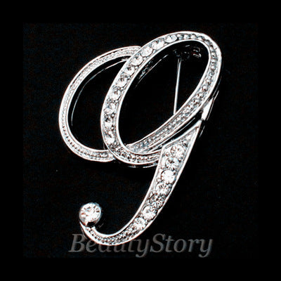 Silver brooch with intricate design letter G on a black background, branded &