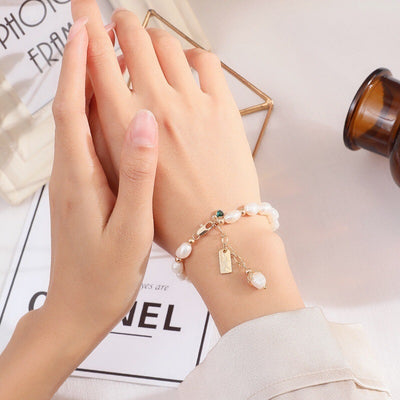 Close-up of hands wearing a pearl bracelet on a light background