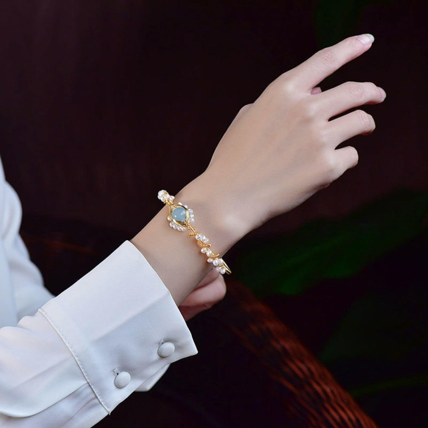 Hand wearing a gold bracelet with a blue gemstone against a dark background