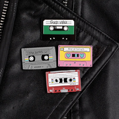 Four cassette tape-shaped pins on a black leather surface