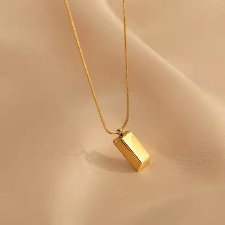 Gold necklace with a rectangular pendant on a beige background