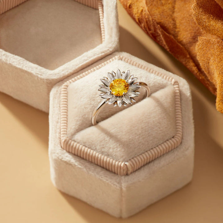 Ring with a yellow gemstone in a hexagonal jewelry box on a beige surface