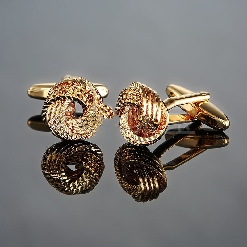 Pair of gold knot cufflinks on a reflective surface with a gray background