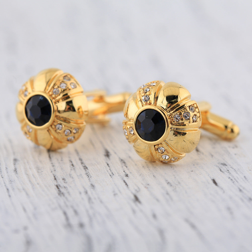 Gold cufflinks with black gemstones on a marble surface