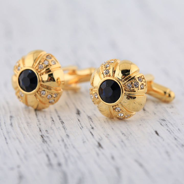 Gold cufflinks with black gemstones on a marble surface