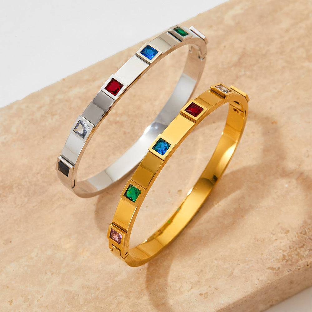 Two bracelets, one gold and one silver, with gemstones on a beige surface.