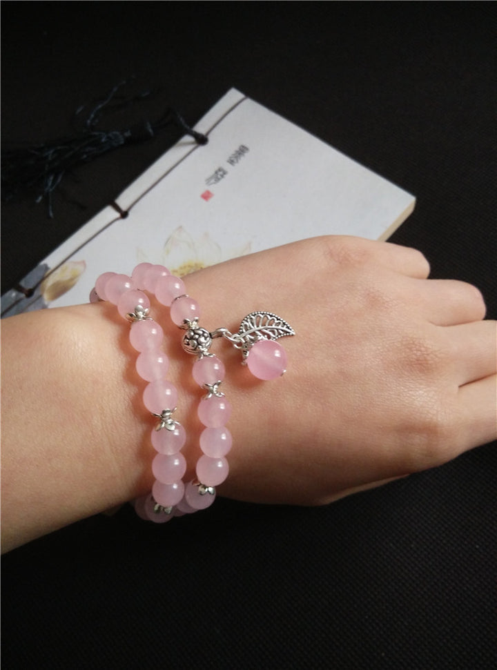 Pink beaded bracelet with silver charms on a wrist against a dark background