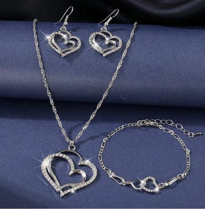 Silver heart-shaped jewelry set including necklace, earrings, and bracelet on a blue fabric background