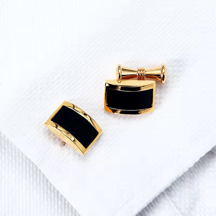 Gold cufflinks with black stones on a white fabric background