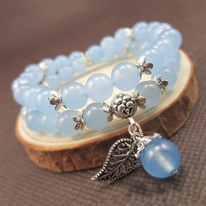 Blue beaded bracelet with silver leaf charm on a wooden stand