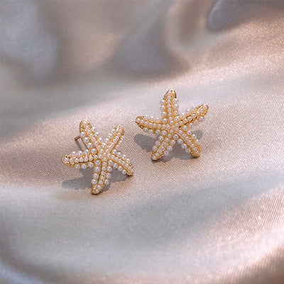 Starfish-shaped earrings with pearls on a soft fabric background