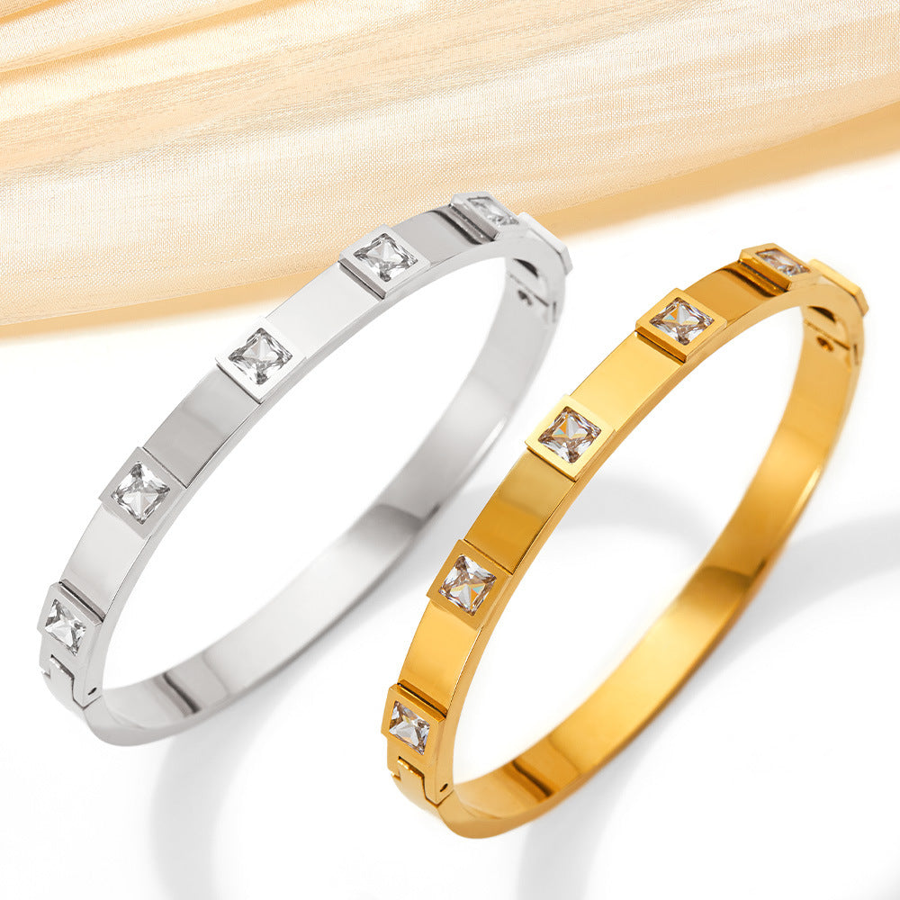 Two bracelets, one silver and one gold, with diamond-like stones on a light wooden background.