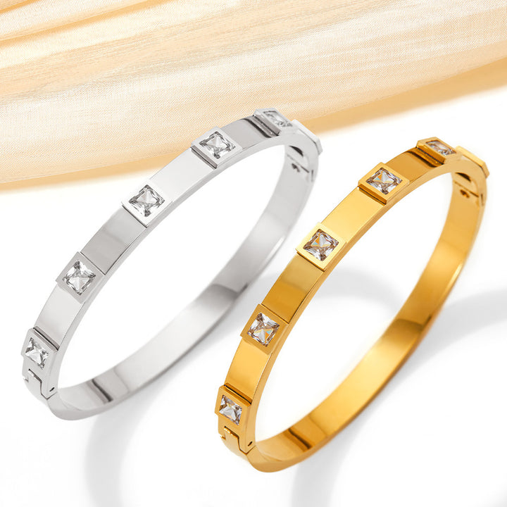Two bracelets, one silver and one gold, with diamond-like stones on a light wooden background.