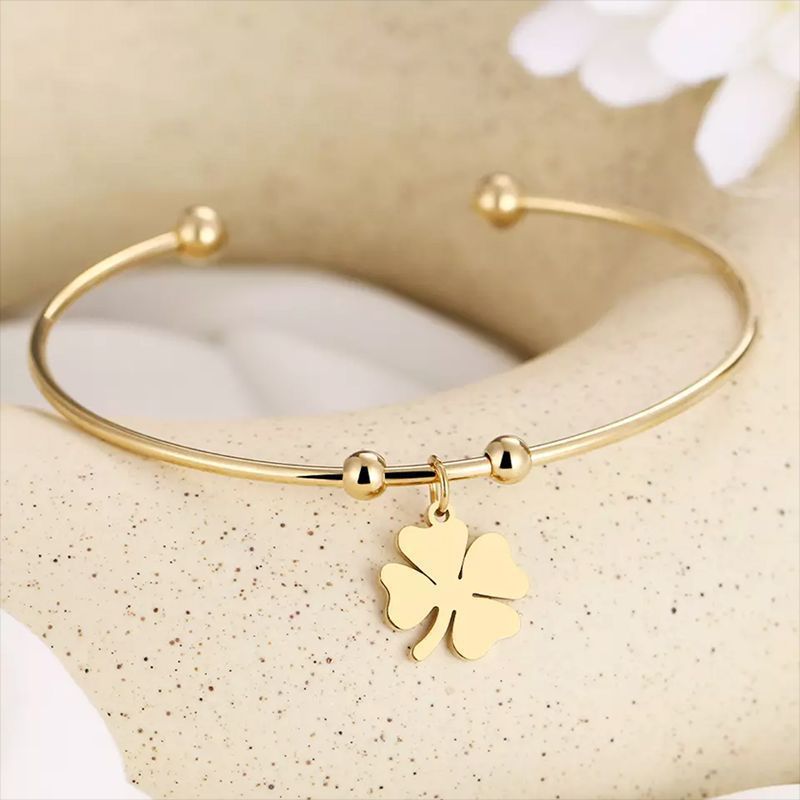 Gold bracelet with a four-leaf clover charm on a beige background