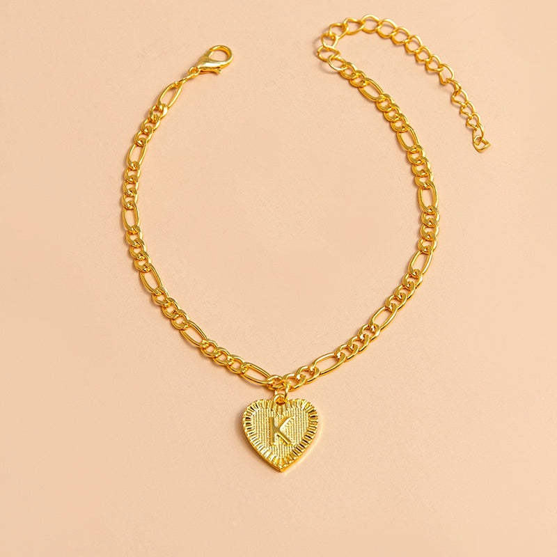 Gold chain necklace with a heart-shaped pendant featuring the letter 'K' on a beige background