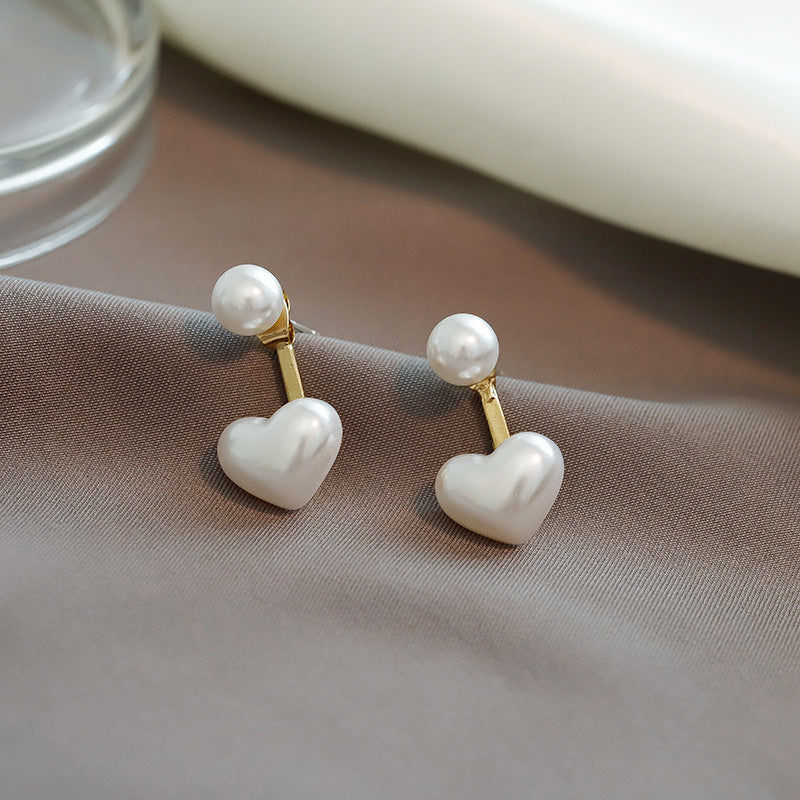 Heart-shaped earrings with pearl tops on a beige fabric background