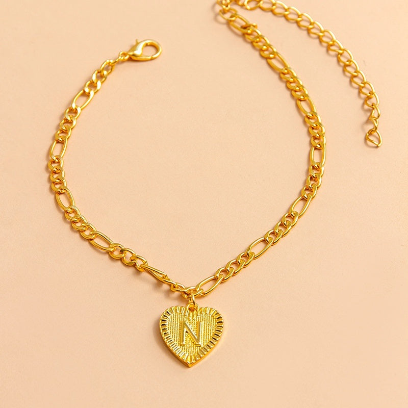 Gold chain bracelet with a heart-shaped pendant letter N on a beige background