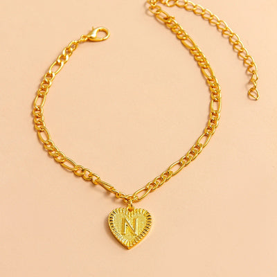 Gold chain bracelet with a heart-shaped pendant letter N on a beige background