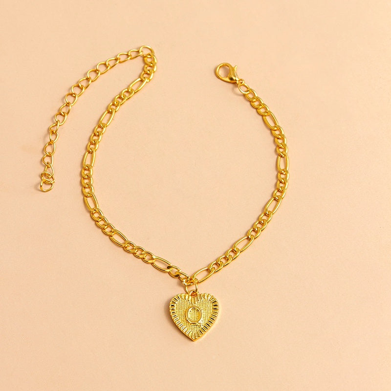 Gold chain bracelet with a heart-shaped pendant letter Q on a beige background