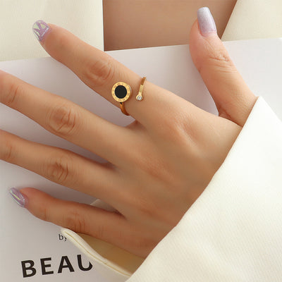 Hand wearing a gold tone ring with a black gemstone on a light background