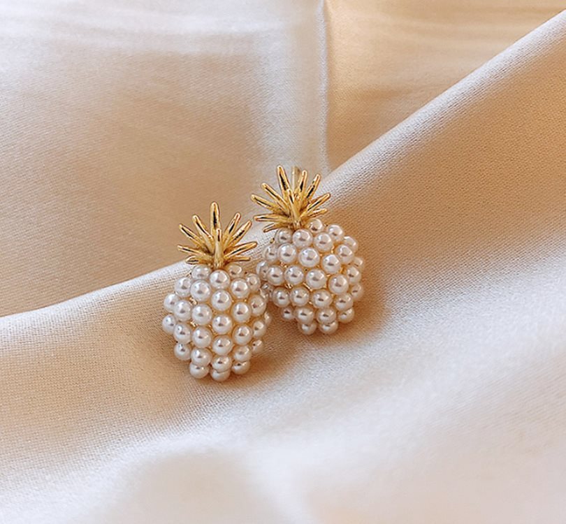 Pearl pineapple-shaped earrings on a beige fabric background