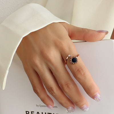 Hand wearing a rose gold tone ring with a black gemstone on a light background