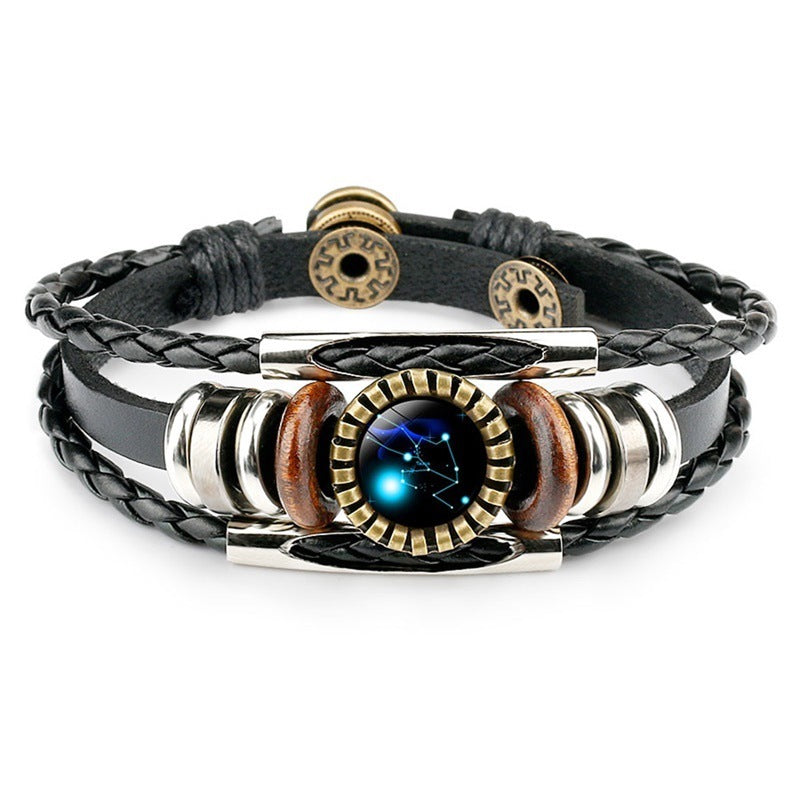 Leather bracelet featuring a blue constellation centerpiece, flanked by silver rings and wooden beads. Braided and smooth black straps add texture.