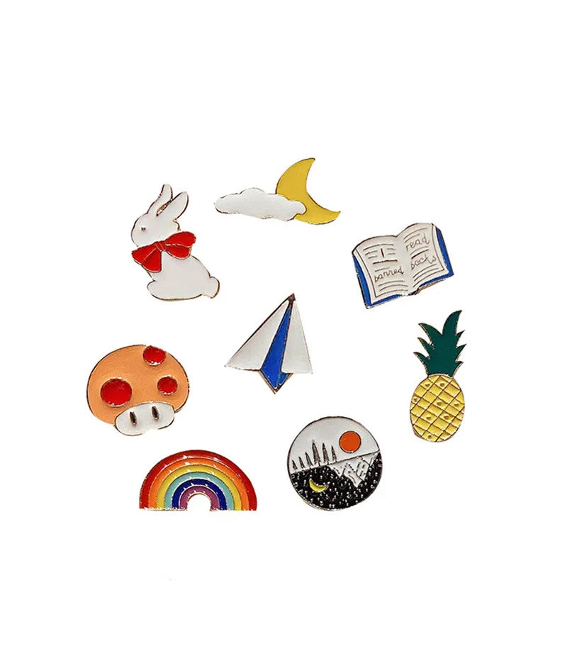 Set of colorful pins including a rabbit, moon, book, mushroom, sailboat, rainbow, pineapple, and moon design on a white background.
