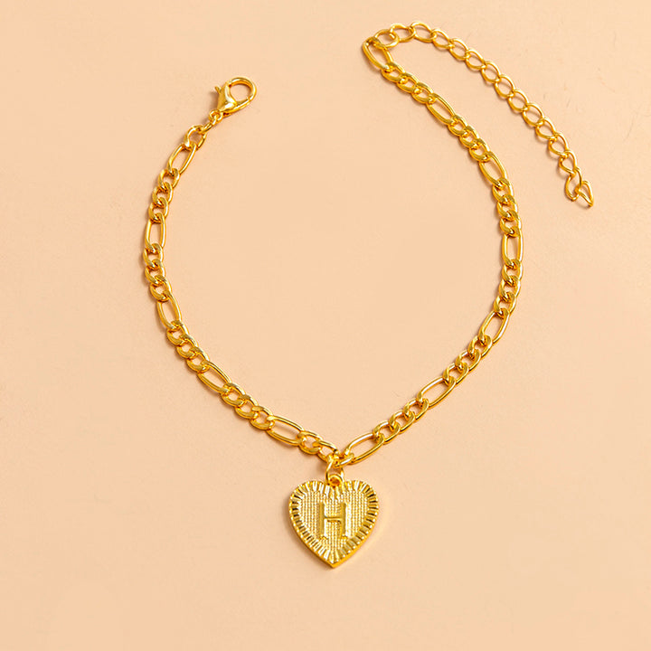 Gold chain bracelet with a heart-shaped pendant letter H on a beige background