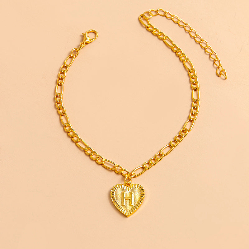Gold chain bracelet with a heart-shaped pendant letter H on a beige background