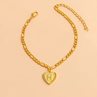 Gold chain bracelet with a heart-shaped pendant letter H on a beige background