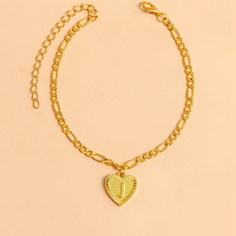 Gold chain necklace with a heart-shaped pendant letter J on a beige background