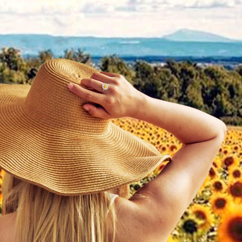 Person wearing aring and straw hat with a scenic background of sunflowers and mountains.
