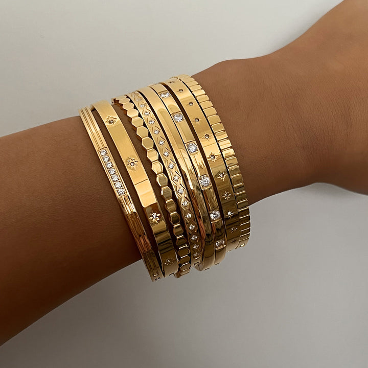Gold bracelets on a wrist against a neutral background