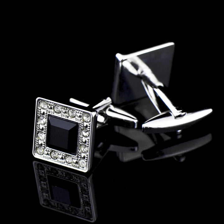 Silver cufflinks with a black square center and clear stones on a black background