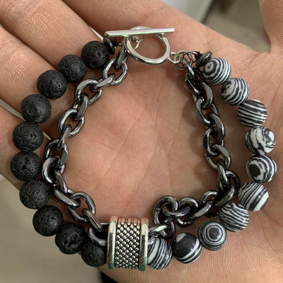 Bracelet with black beads, silver chain, and striped beads on a hand.