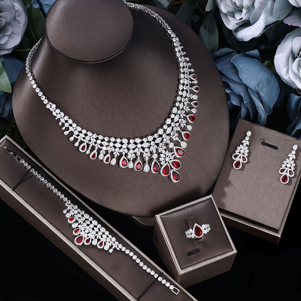 Red gem Jewelry set including necklace, earrings, bracelet and ring on a brown jewelry box with flowers in the background.