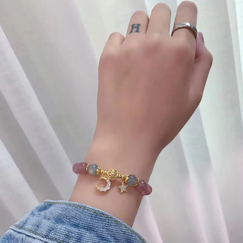 Hand wearing a bracelet with colorful beads and charms against a white background