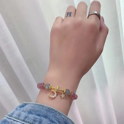 Hand wearing a bracelet with colorful beads and charms against a white background