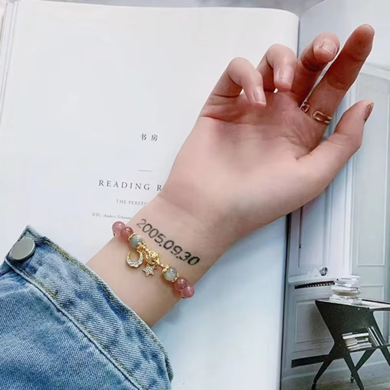 Hand with bracelet and tattoo on wrist, open book in background