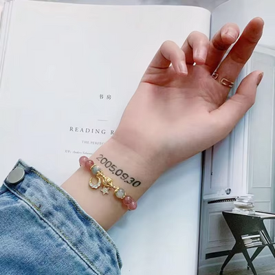 Hand with bracelet and tattoo on wrist, open book in background