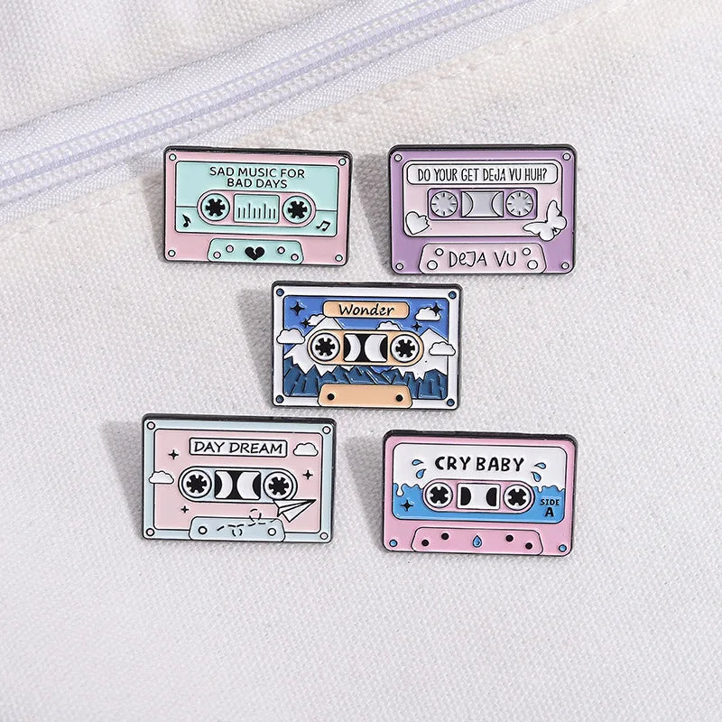 Five cassette tape-shaped pins with different designs and text on a white background